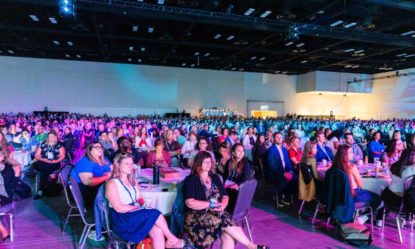 Many people sitting in chairs in a conference room with a purple floor and a white ceiling.