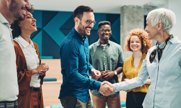 Group of people shaking hands with one another, smiling, and laughing in a meeting room.