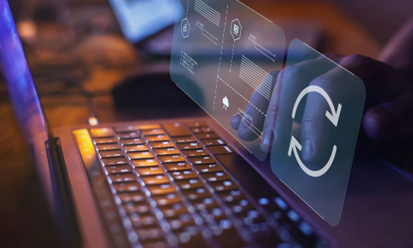 Hands holding a screen with a refresh button over a laptop keyboard in a dimly lit room.