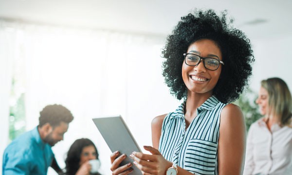 A smiling woman with glasses holds a tablet, showcasing her engagement with technology.