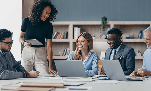 A diverse group of professionals engaged in a meeting around a table with laptops, discussing ideas and collaborating.