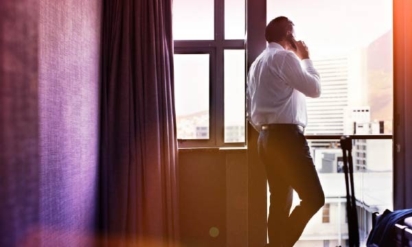 A man stands by a window, talking on his phone, gazing thoughtfully outside into the distance.