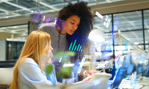 Two professionals collaborate at a desk, surrounded by digital charts and graphs, highlighting data analysis in a modern office setting.