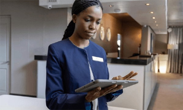 A professional staff member in a blue uniform holds a tablet, ready to assist in a stylish, modern reception area.