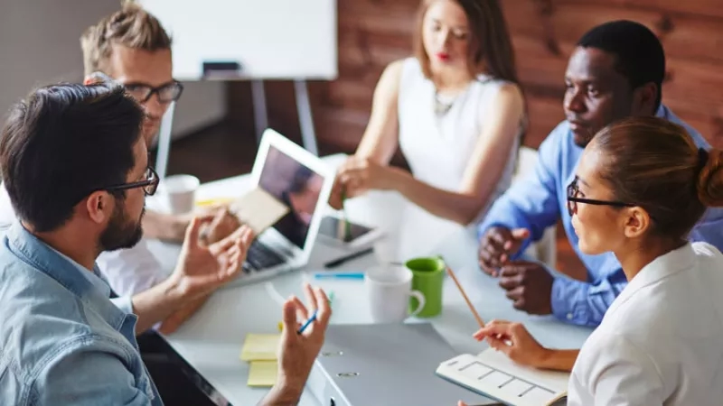 A group of business people are having a meeting and discussing something while sitting around a table.