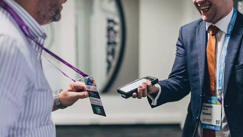 A man wearing a badge scanning another man's badge at a conference.