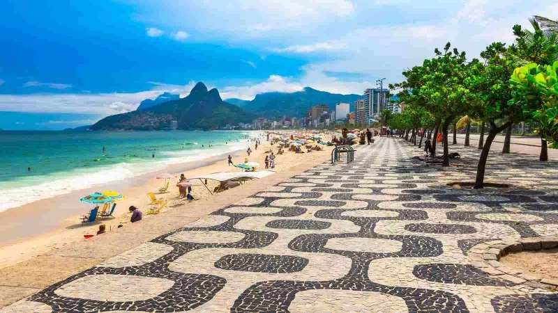 Copacabana beach, Rio de Janeiro, Brazil with people, umbrellas, buildings, and mountains in the distance.