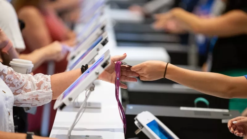 A woman is scanning her badge at a table, while another woman is looking on.