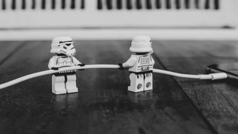 Two Lego Star Wars stormtroopers connected by a cable to a cell phone on a wooden table.