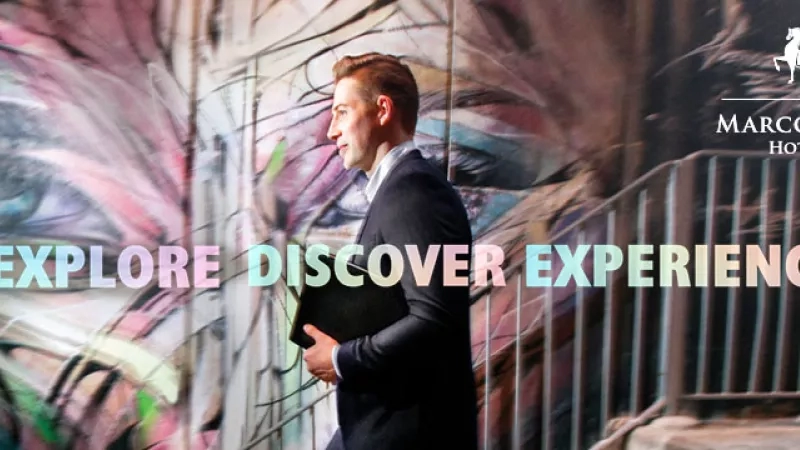 Marco Polo Hotels: Explore, Discover, Experience. Man in suit in front of a colorful mural.