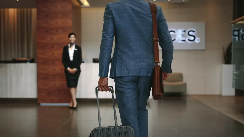 Man with luggage at hotel lobby with sign in background that says aces