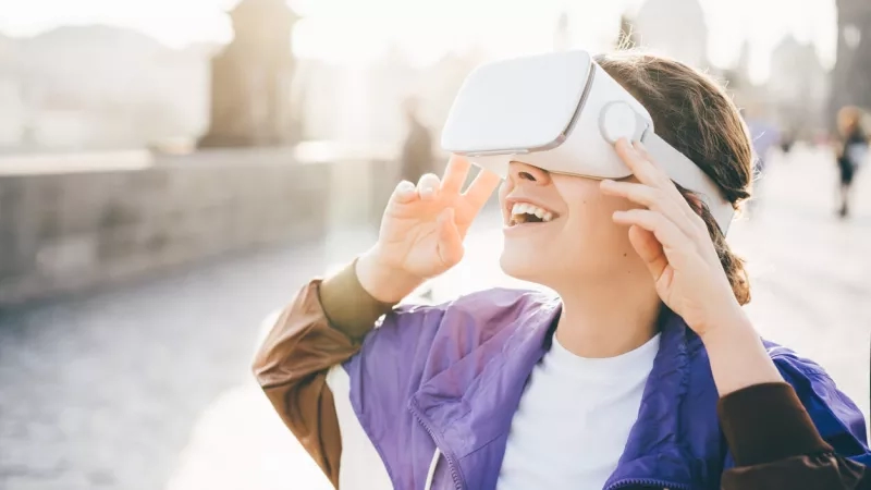 Woman wearing purple jacket using VR headset for virtual tourism in front of blurred cityscape.