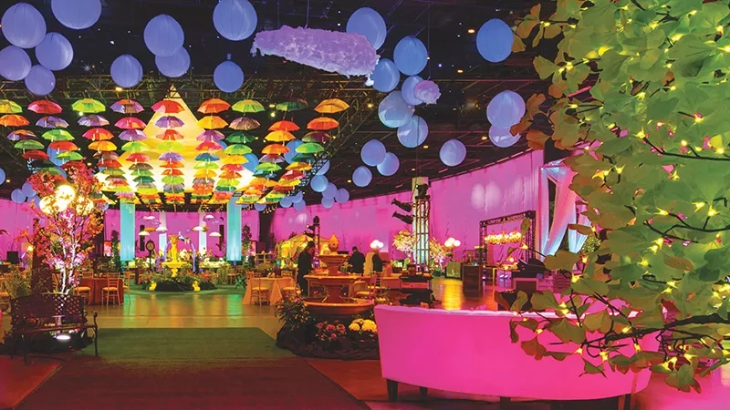 Party hall with a pink-themed setup, balloons, and an illuminated, vibrant ambiance with a green plant.