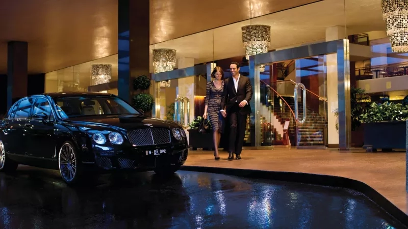 A Bentley car parked in front of a hotel with a couple walking hand in hand.
