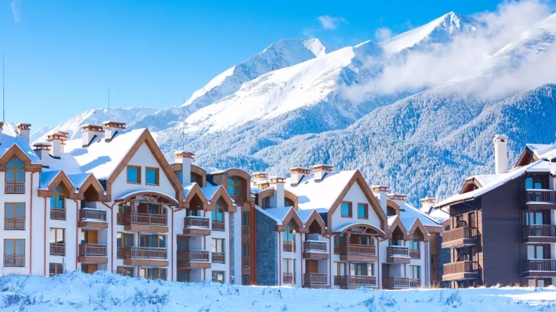 Buildings with snow on the roofs and mountains in the background under a blue sky with clouds.