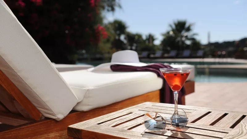 Close-up of a drink by a pool at a luxury hotel, with sunglasses on a wooden table.