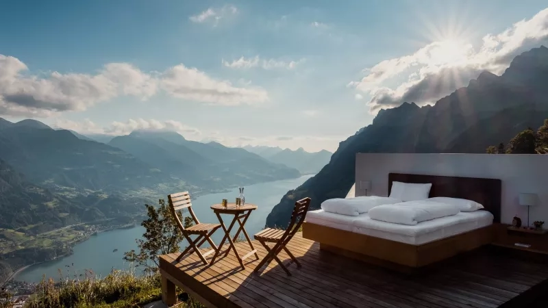 Outdoor bedroom with a bed, table, chairs, and a lake view.