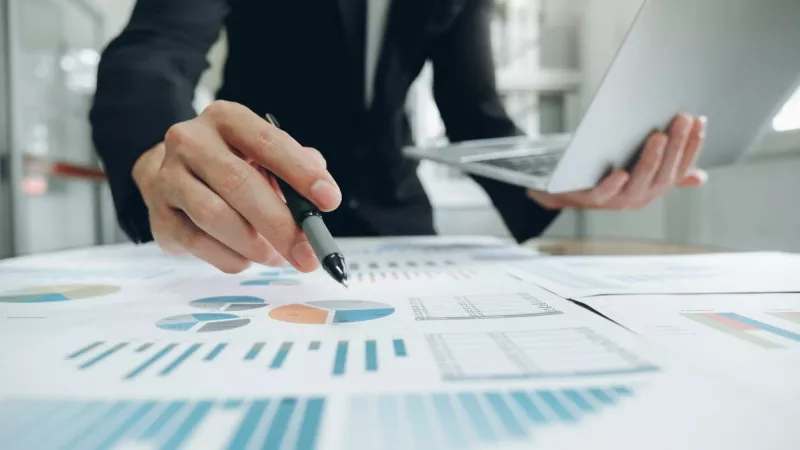 Businessperson analyzing revenue management data on computer and spreadsheet in a blurred office.