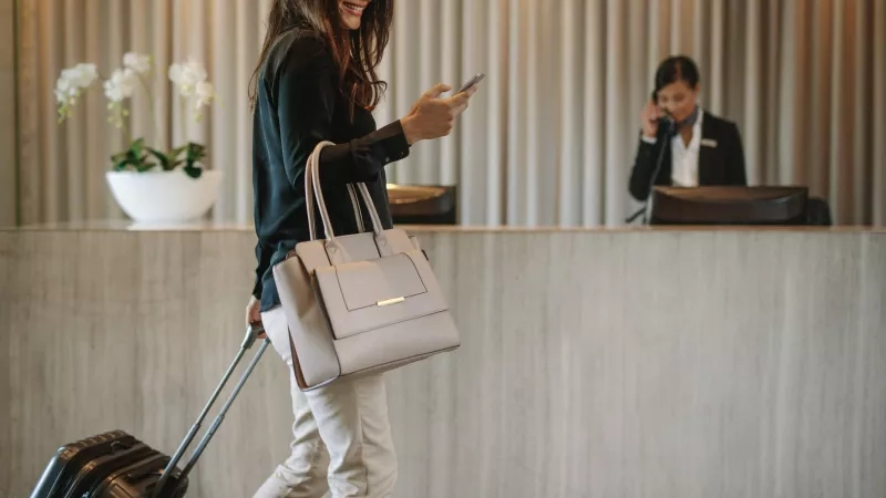 Business traveler walking through hotel lobby with suitcase smiling at phone