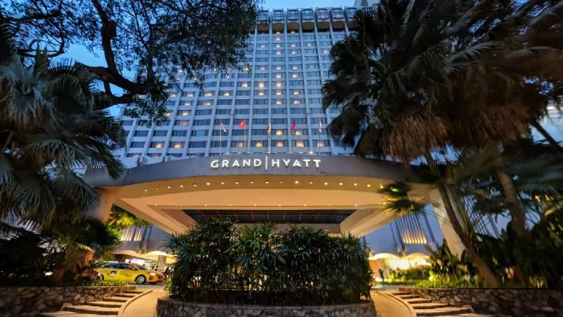 Exterior view of the Grand Hyatt Singapore with lush landscaping and a glowing entrance at night.