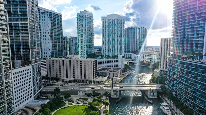 A top-down view of buildings and a river with a bridge, cars, trees, and a yacht.