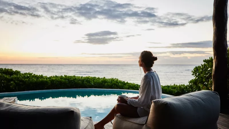 A woman sitting on a beanbag chair at a tropical resort, enjoying the ocean view at sunset.
