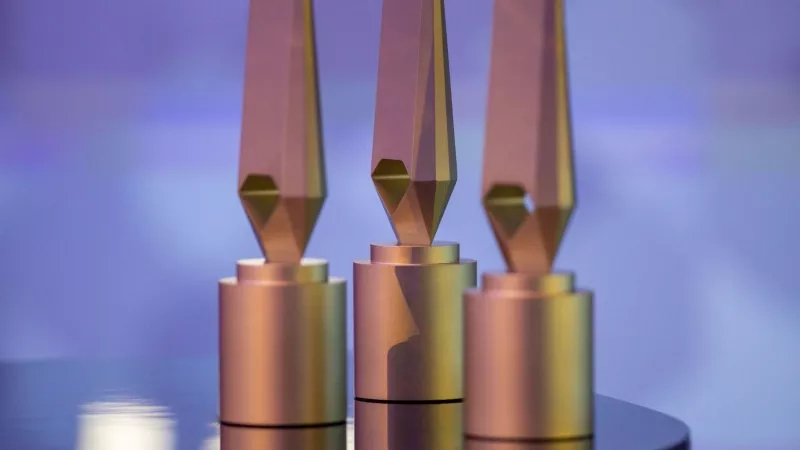 Three golden awards on a table with a purple background, showcasing a sleek and modern design.