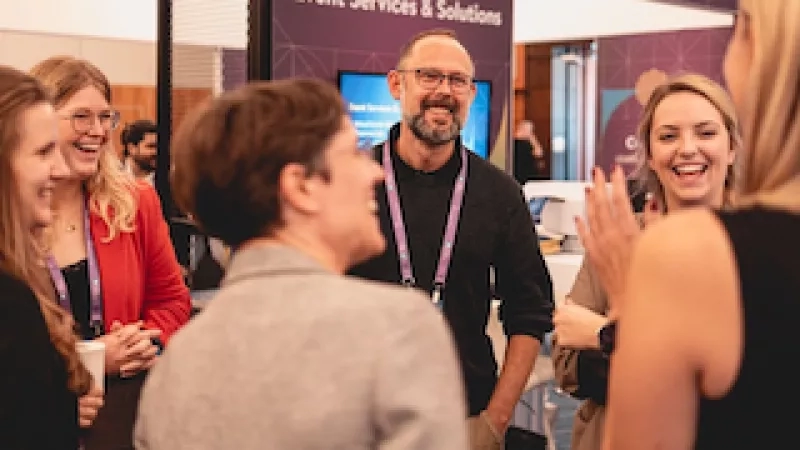 A group of people chatting in front of a large screen at an event.