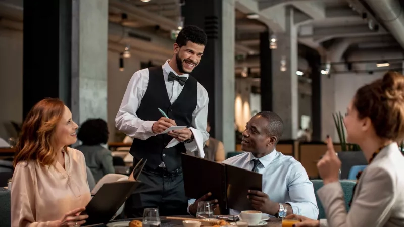 Group of people dining in a restaurant with a server taking orders, and a warm ambiance.