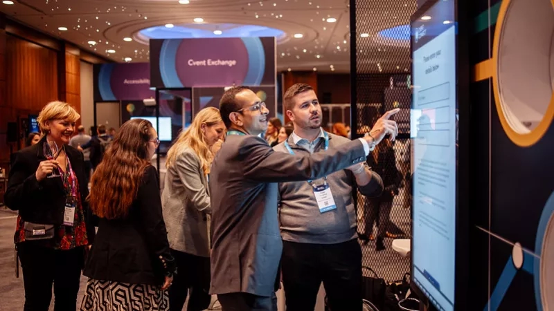 Two men point at a touch screen display at the 2023 Cvent Connect conference in National Harbor, Maryland.