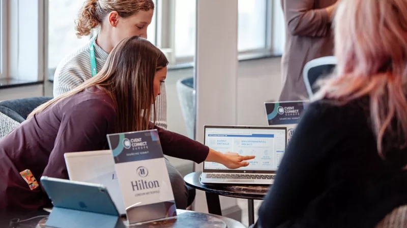 Three women at a conference, using a laptop, with Hilton and Cvent Connect branding present in the image.