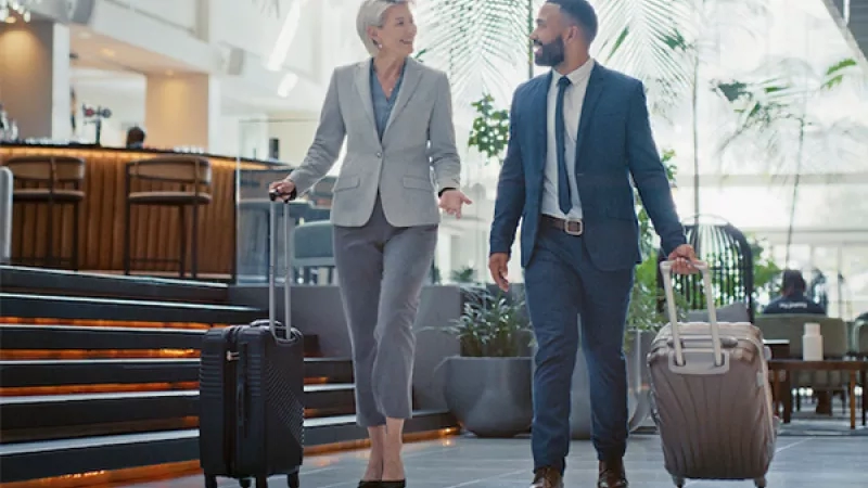 Two people in business attire with luggage walking in an airport lounge at the Hotel Data UK.