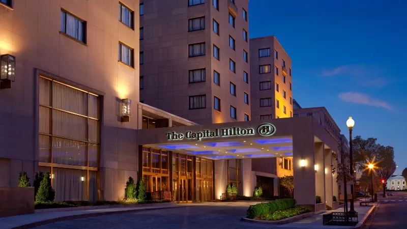 Capital Hilton exterior with illuminated signage at night with landscaping and street lights in the foreground.