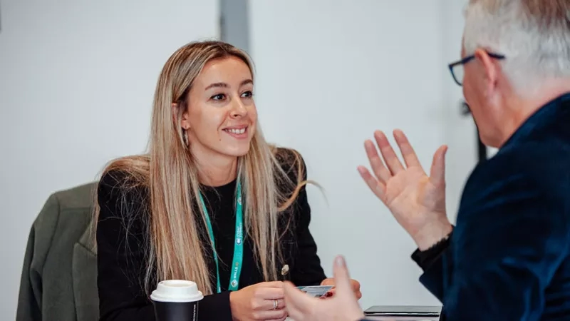 A man and a woman sitting at a table having a discussion in a professional setting.
