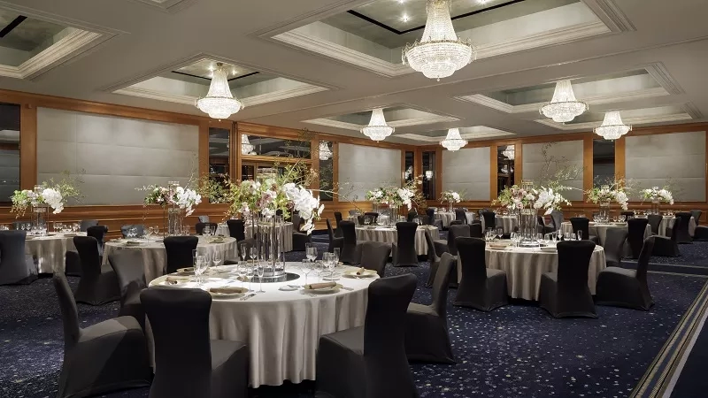 A luxurious ballroom at W Singapore Sentosa Cove with round tables and chandeliers.