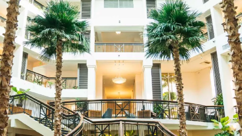 A white building with balconies, trees, a spiral staircase, and a chandelier in the center.