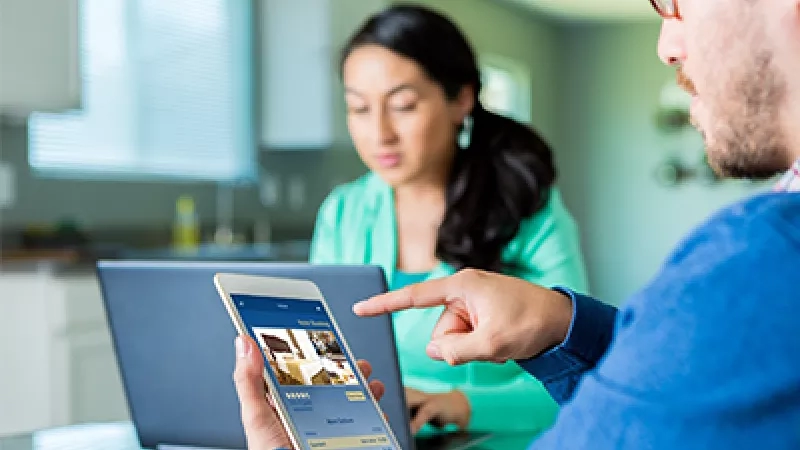 A man showing a woman a room block on a mobile phone in a kitchen.