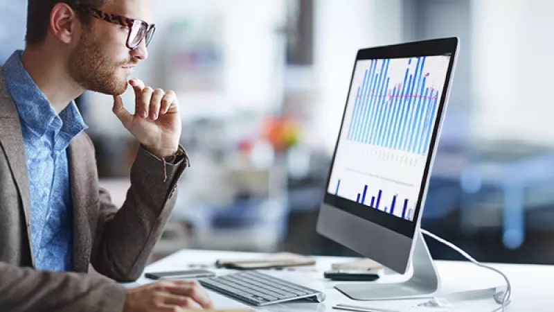 Businessman looking at computer screen with graph chart on it, pondering how to skyrocket revenue.