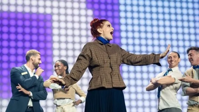 A group of people performing on stage in front of a purple and blue square background.