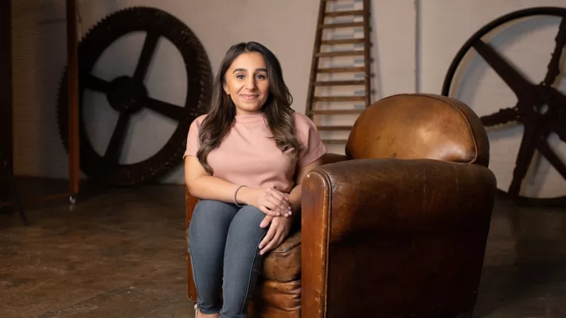 Woman sits in a chair with gears on the wall behind her and a ladder to the side.