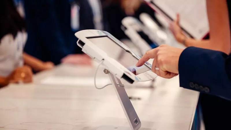 Person touches a tablet while other people sit at a counter at a trade show.