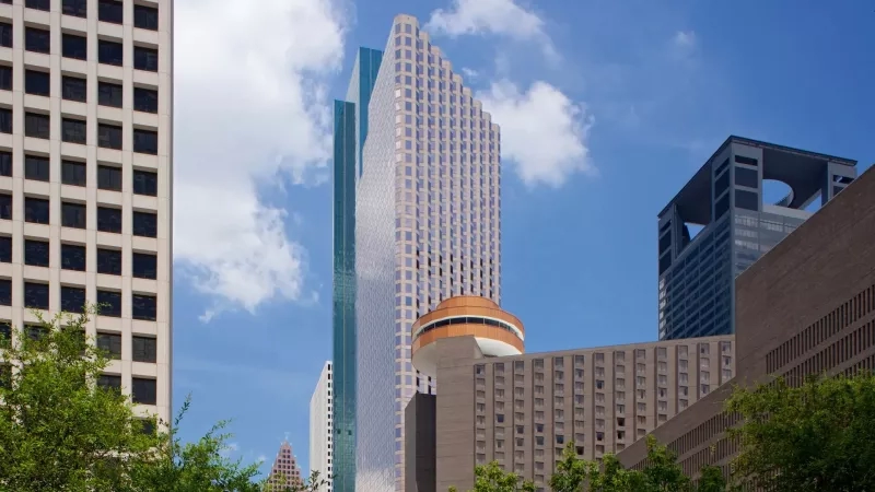 Hyatt Regency Houston Downtown, a tall building in an urban city with other skyscrapers and lush trees.