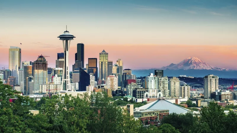 A view of the Seattle skyline and the Space Needle at sunset, with lush greenery in the foreground.