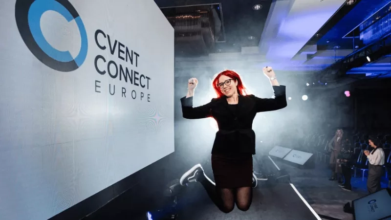 A woman jumps in the air with the words "Cvent Connect Europe" on the wall behind her.