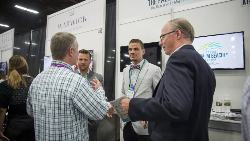 Three men and one woman are standing in front of a wall with a Discover Palm Beaches logo.