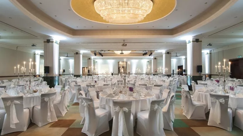 Ballroom at Sofitel Brussels Europe with round tables and chairs, a large chandelier, and lit candles.