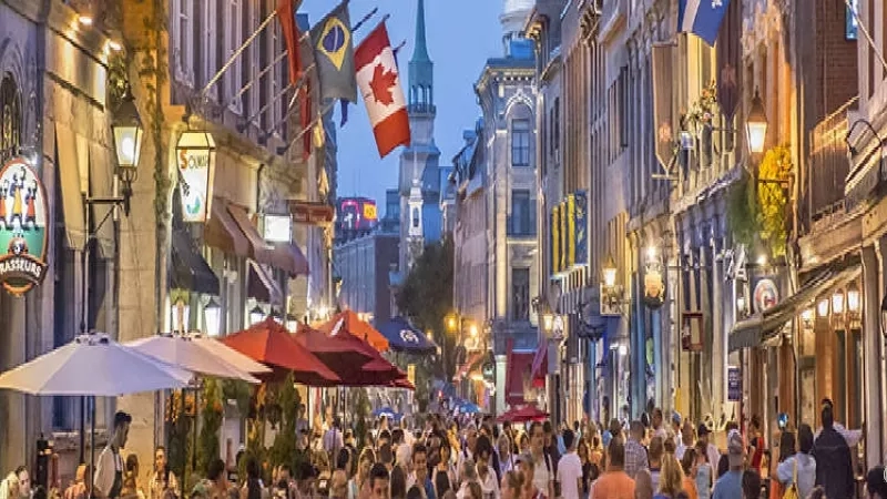 A crowded street at night with many people, flags, buildings, and umbrellas in Montreal, Quebec.