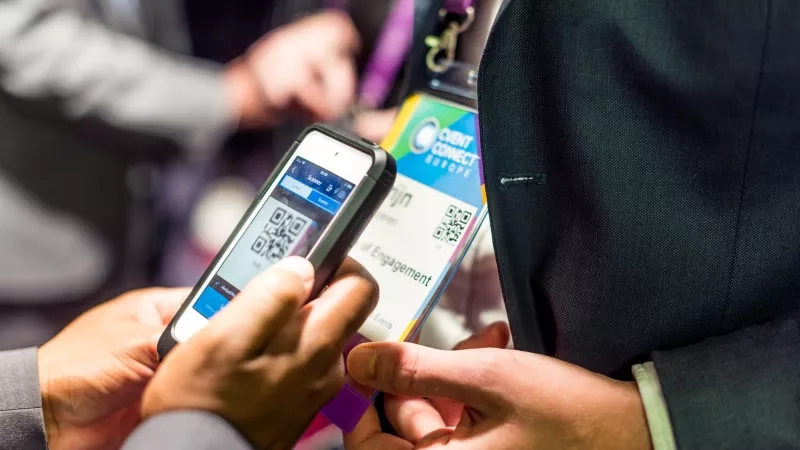 Two people are exchanging contact information using QR codes from their phones and business cards.