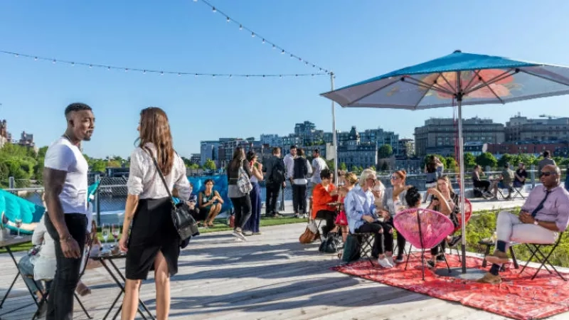 People are standing and sitting under umbrellas on a wooden deck at the Montreal hotel.