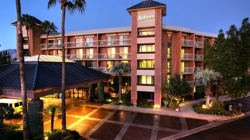Exterior view of Radisson Hotel Tucson at dusk with palm trees and other landscaping features.